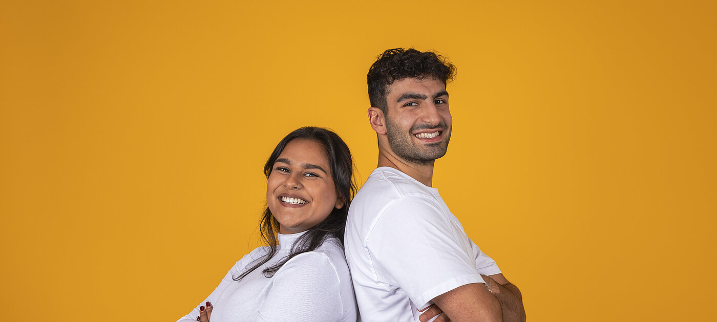 zwei junge Menschen stehen Rücken an Rücken und lächeln